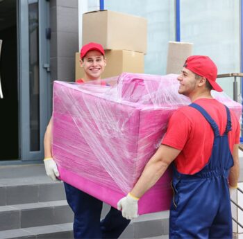 Umzug in Kleve Zwei Umzugshelfer tragen ein in Folie gepacktes Möbelstück – Umzug in Kleve