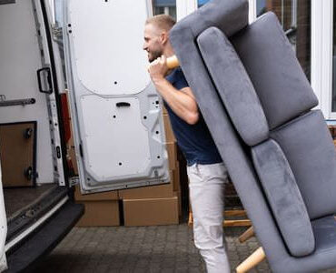 Möbellift Kleve Möbellift Kleve: Helfer tragen ein graues Sofa aus einem Transporter